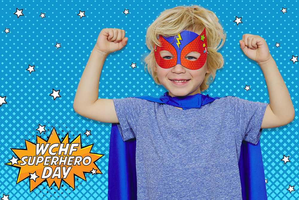 Young blonde boy smiling in superhero costume posing with fists up