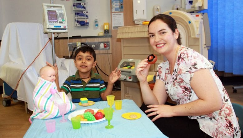 Young child in Hospital playing with doll and engaging with Play Therapist.