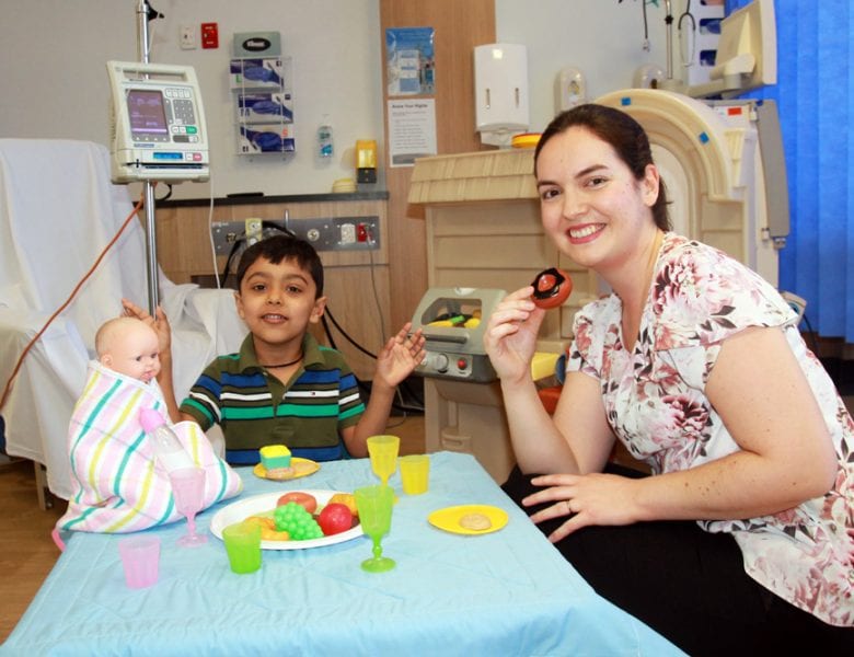 Young child in Hospital playing with doll and engaging with Play Therapist.
