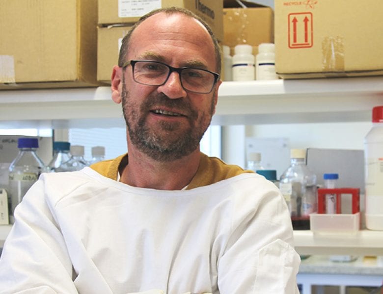 Man wearing white lab coat crossing arms smiling at camera