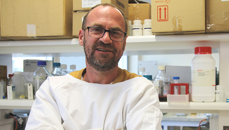 Man wearing white lab coat crossing arms smiling at camera