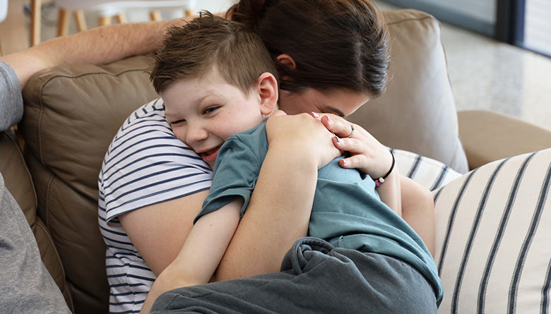 Young patient Declan in am embrace with his mum on a couch at the WCH Foundation Beach House.