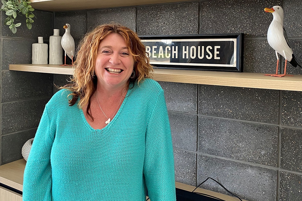 Cheryl Minniss standing in front of Beach House sign at the Beach House. 