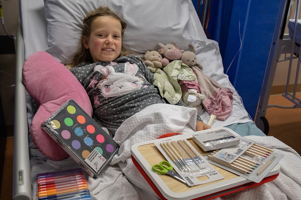 Girl in hospital bed with craft supplies presents.