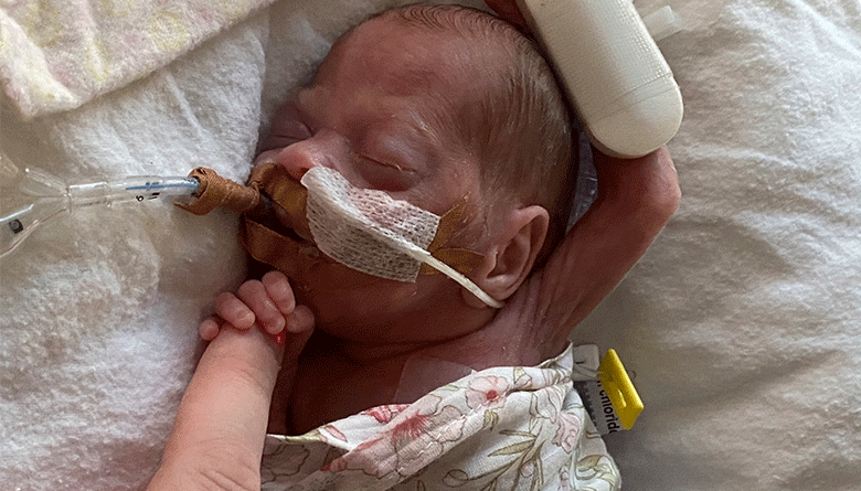 Charlee holding her Mother's finger in her NICU cot