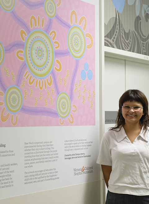 Tanaya Antony standing beside her artwork 'At the Heart of Healing' in Rose Ward at the Women's and Children's Hospital.